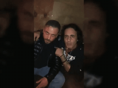 Two Men Sitting, One In S.A. Shirt GIF