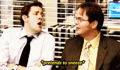 Two Men Sitting One Pretending To Sneeze GIF