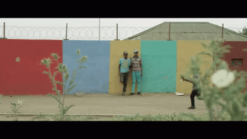 Two Men Stand In Front Of A Colorful Wall With Barbed Wire GIF