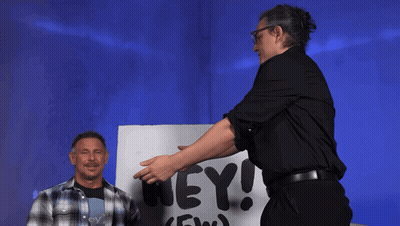Two Men Stand In Front Of A Sign That Says Aew Hey GIF