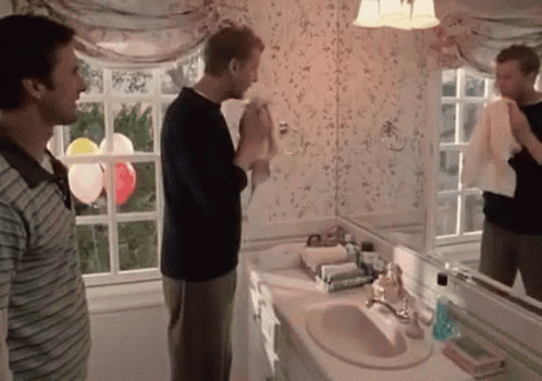 Two Men Standing In A Bathroom With Balloons In The Window GIF