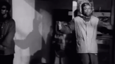 Two Men Standing In Black And White Room GIF