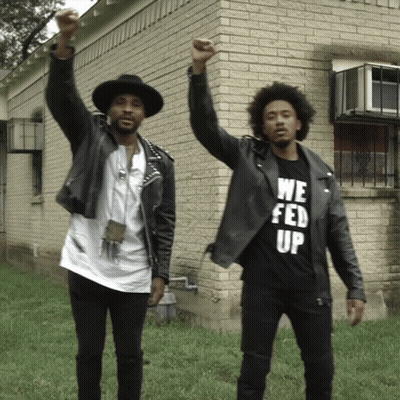 Two Men Standing In Front Of A Brick Building One Wearing A We Fed Up T-Shirt GIF