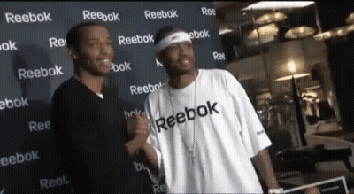 Two Men Standing In Front Of A Wall That Says Reebok On It GIF