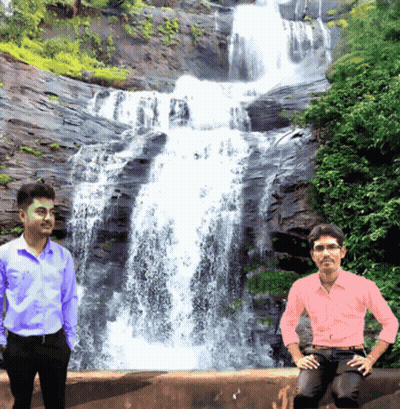 Two Men Standing In Front Of A Waterfall With One Wearing A Pink Shirt GIF