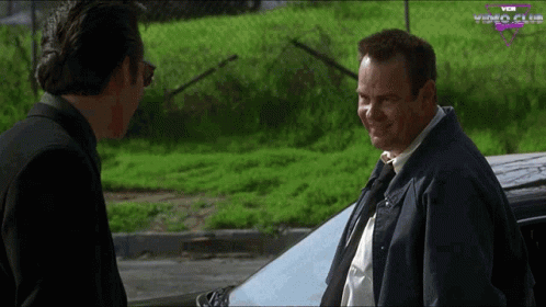 Two Men Standing In Front Of Car With Video Club GIF