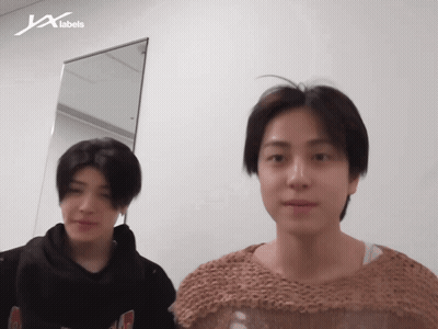 Two Men Standing In Front Of JX Labels Wall GIF