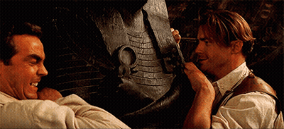 Two Men Standing In Front Of Large Statue GIF