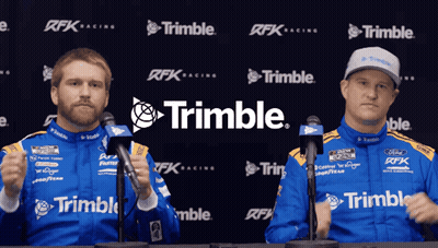 Two Men Standing In Front Of Microphones In Front Of A Trimble Logo GIF