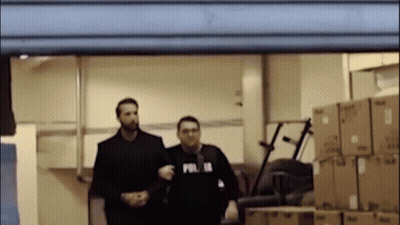 Two Men Standing In Room With Boxes, One Wearing Polis Shirt GIF