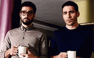 Two Men Standing Next To Each Other Holding Cups Of Coffee . GIF
