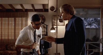 Two Men Standing Next To Each Other In A Room With A Lamp GIF