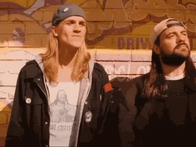 Two Men Standing Next To Each Other In Front Of A Wall With Graffiti On It That Says Drive GIF