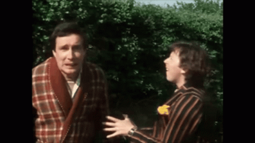 Two Men Standing Next To Each Other In Front Of Hedge GIF