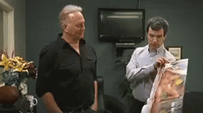 Two Men Standing Next To Each Other Looking At Bag Of Chips GIF