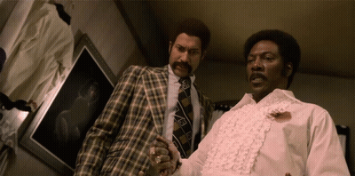 Two Men Standing Next To Each Other With One Wearing A White Shirt With Ruffles On The Sleeves GIF