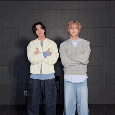 Two Men Standing Next To Each Other With Their Arms Crossed In Front Of A Wall With The Letter B On It GIF