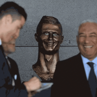 Two Men Standing Next To Man's Head Statue GIF