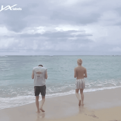 Two Men Standing On A Beach With A Label That Says Labels On It GIF