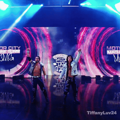 Two Men Standing On A Stage In Front Of A Screen That Says Top City GIF