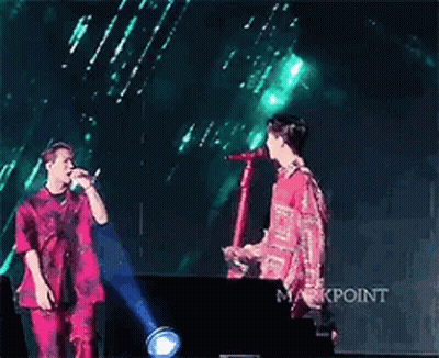 Two Men Standing On Stage Holding Microphone GIF
