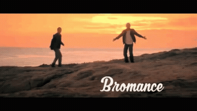 Two Men Standing On Top Of A Sandy Hill With The Word Bromance Written Below Them GIF