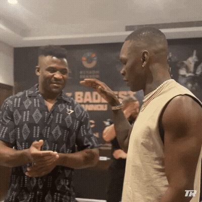 Two Men Talking In Front Of Bad Ass Sign GIF