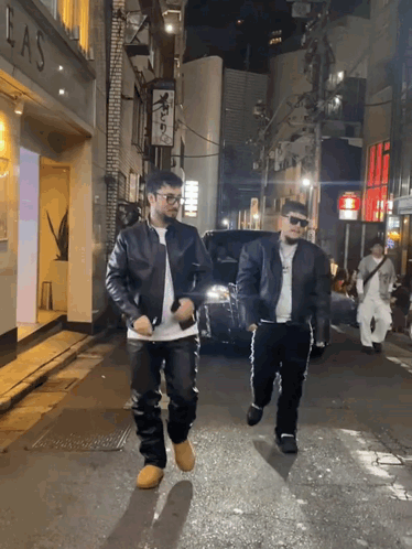 Two Men Walking Down A Street With A Sign That Says Las GIF