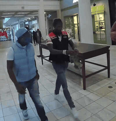Two Men Walking In A Mall With One Wearing A Shirt That Says ' Columbia ' On It GIF