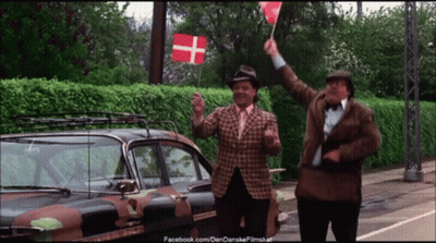 Two Men Waving Flags In Front Of A Camouflage Car With Facebook.com On The Bottom Right GIF