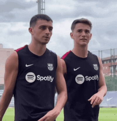 Two Men Wearing Black Spotify Shirts Stand Next To Each Other GIF