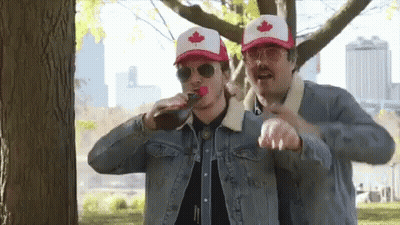 Two Men Wearing Canadian Hats And Sunglasses Are Drinking From A Bottle . GIF
