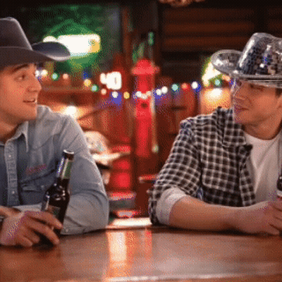 Two Men Wearing Cowboy Hats Are Sitting At A Bar Talking GIF