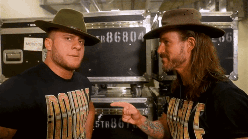 Two Men Wearing Cowboy Hats Are Standing Next To Each Other With One Wearing A Shirt That Says ' Down ' On It GIF