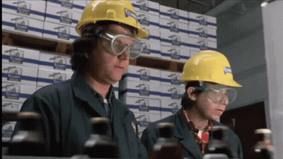Two Men Wearing Hard Hats And Safety Goggles Are Looking At Bottles In A Warehouse With Boxes Of Clampy In The Backgroun GIF