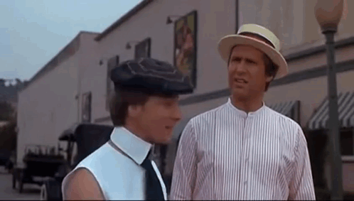 Two Men Wearing Hats And Ties Are Standing Next To Each Other On A City Street . GIF