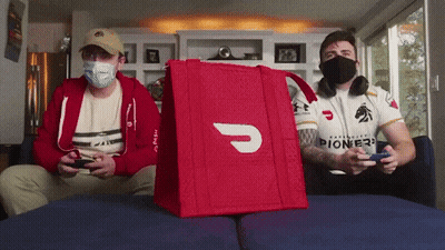 Two Men Wearing Masks Are Playing A Video Game With A Red Bag That Says Pioneer On It GIF
