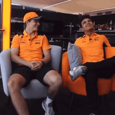 Two Men Wearing Orange Shirts Are Sitting In Chairs And Talking . GIF
