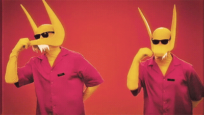 Two Men Wearing Pink Shirts And Yellow Masks With Horns Are Standing Next To Each Other On A Red Background GIF