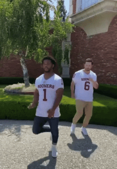 Two Men Wearing Sooners Jerseys Are Dancing On The Sidewalk GIF