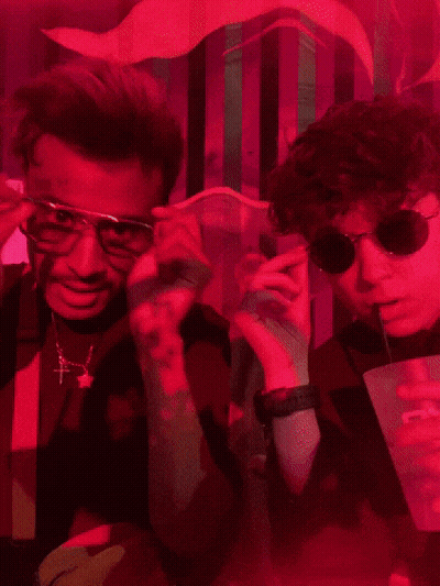 Two Men Wearing Sunglasses And Suspenders Pose For A Picture In A Dark Room GIF
