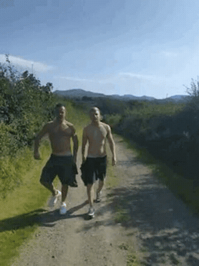 Two Men Without Shirts Are Walking Down A Dirt Road . GIF