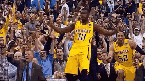 Two Michigan Basketball Players Are Celebrating In Front Of A Crowd . GIF