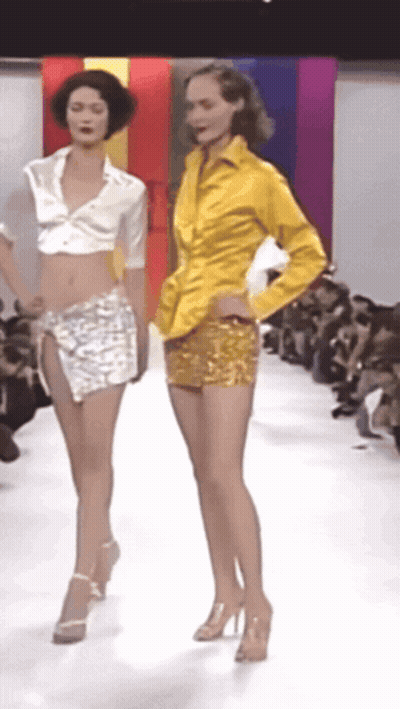 Two Models Are Walking Down A Runway Wearing Shorts And A Yellow Shirt GIF