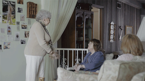 Two Older Women Are Talking In A Living Room With A Poster On The Wall That Says " Why I Need " GIF