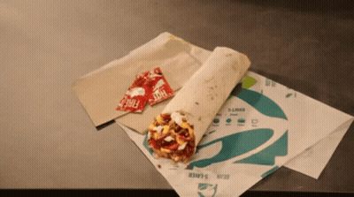 Two Packets Of Hot Sauce Sit Next To A Taco Bell Burrito GIF