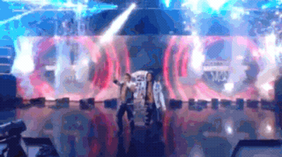 Two People Are Dancing On A Stage In Front Of A Large Screen That Says ' A ' On It . GIF