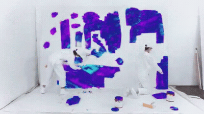 Two People Are Painting On A White Wall With Purple And Blue Paint . GIF