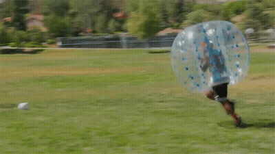 two people are playing bubble soccer in a field