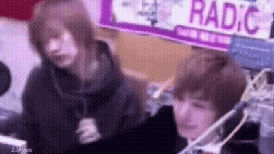 Two People Are Sitting In Front Of A Microphone In A Room . GIF